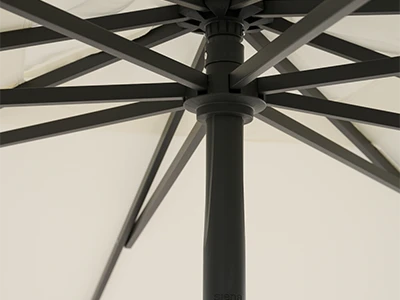 Blick von unten auf die dunklen Streben und den Mast eines geöffneten Sonnenschirms mit hellem Stoff.