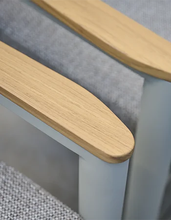 Detailaufnahme einer Gartenstuhl Armlehne aus hellem Holz mit hellgrauem Metallrahmen und gepolsterter Sitzfläche.