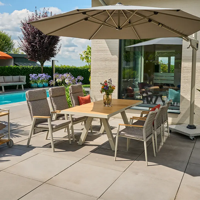 Moderne Outdoor Essgruppe mit gepolsterten Stühlen und Holztisch unter einem großen Sonnenschirm auf einer Terrasse am Pool.