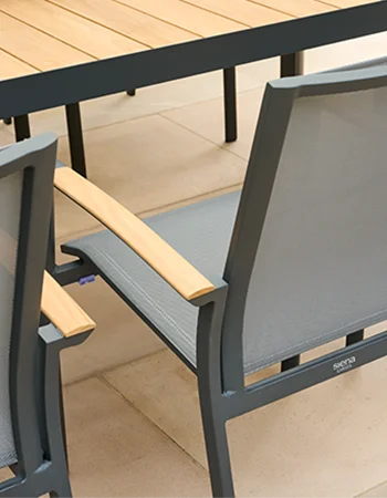 Nahaufnahme eines Gartenstuhls mit grauem Metallrahmen, grauer Textilbespannung und Armlehne aus hellem Holz, daneben die Kante eines Outdoor Tisches mit Holzplatte.