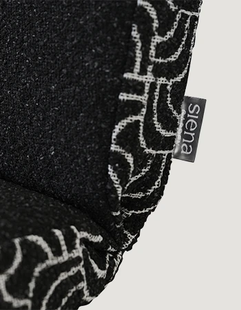 Detailaufnahme einer schwarzen Sitzauflage mit weiß gemustertem Rand und kleinem seitlichem Logo-Etikett vor hellem Hintergrund.