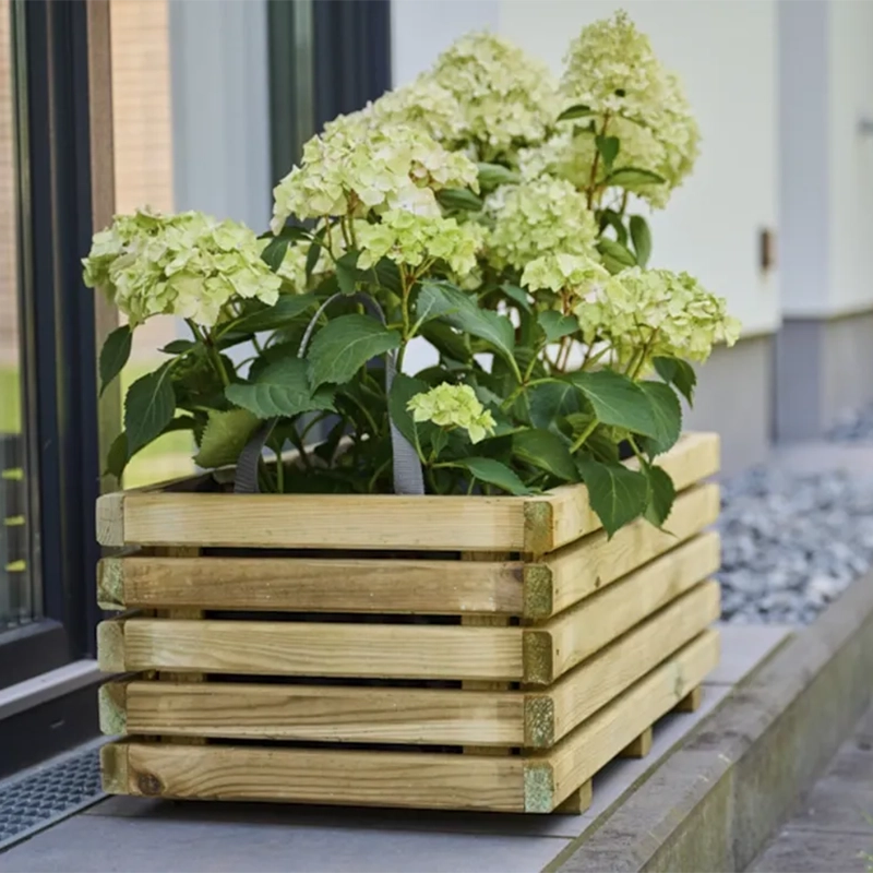 Holz Pflanzkasten mit blühender Hortensie auf einem schmalen Kiesbett neben einer Hauswand und Fensterfront.