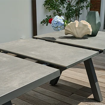 Detailaufnahme eines ausziehbaren Outdoor Tisches mit grauer Tischoberfläche und Dekoobjekten auf einer Holzterrasse.