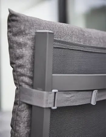 Detailaufnahme einer grauen Sitzauflage mit verstellbarem Halteband auf einem Metallstuhl mit einer Rückenlehne aus luftdurchlässigem Mesh-Gewebe. 