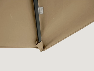 Detail der Schirmspitze eines beigefarbenen Ampelschirms mit sichtbarem Etikett und dunkler Strebe.