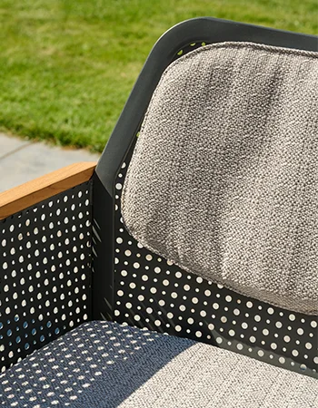 Detailaufnahme eines Outdoor Stuhls mit perforierter Metalllehne, grauen Polstern und Holzarmlehne.