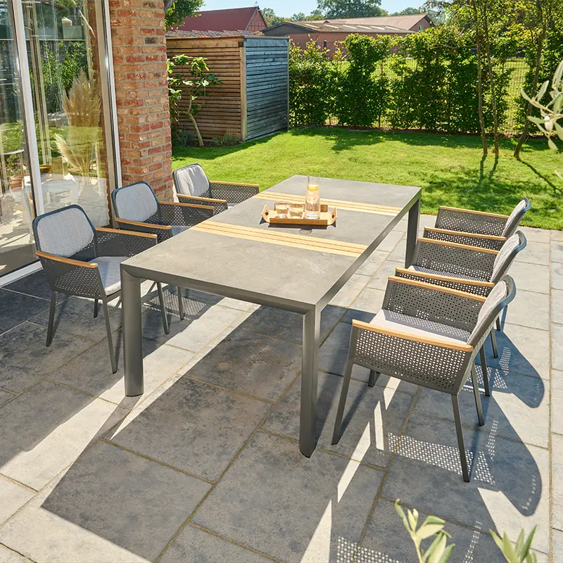 Outdoor Essgruppe mit großem grauen Tisch und sechs gepolsterten Metall Geflechtstühlen auf einer Terrasse im Garten.