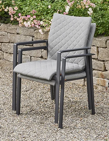 Gestapelte Outdoor Stühle mit grauer Stepp Polsterung und schwarzem Metallgestell vor einer Steinmauer.