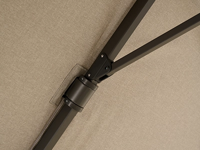 Detailaufnahme eines Gelenks an einer dunklen Schirmstrebe unter beigefarbener Schirm-Bespannung.