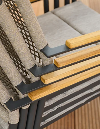 Gestapelte Outdoor Stühle mit grauem Geflecht, hellen Sitzpolstern und Holzarmlehnen auf Metallgestell.