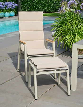 Heller Outdoor Hochlehner mit passendem Fußhocker und Polstern auf einer Terrasse neben dem Pool.