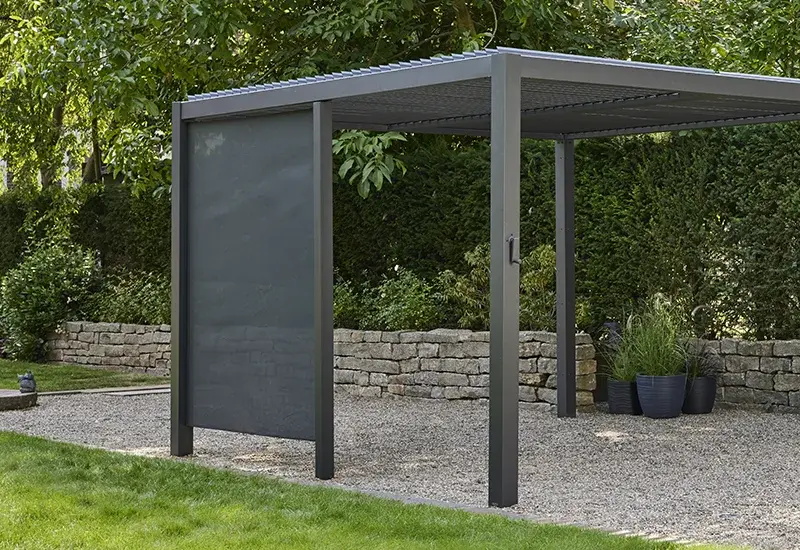 Pergola mit seitlicher, dunkelgrauer, semitransparenten Textilblende als Sonnen- und Sichtschutz in einem Garten.
