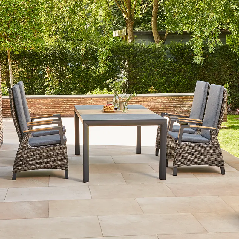 Outdoor Essgruppe mit vier hohen Geflechtstühlen, grauen Polstern und rechteckigem Tisch auf einer Terrasse im Garten.