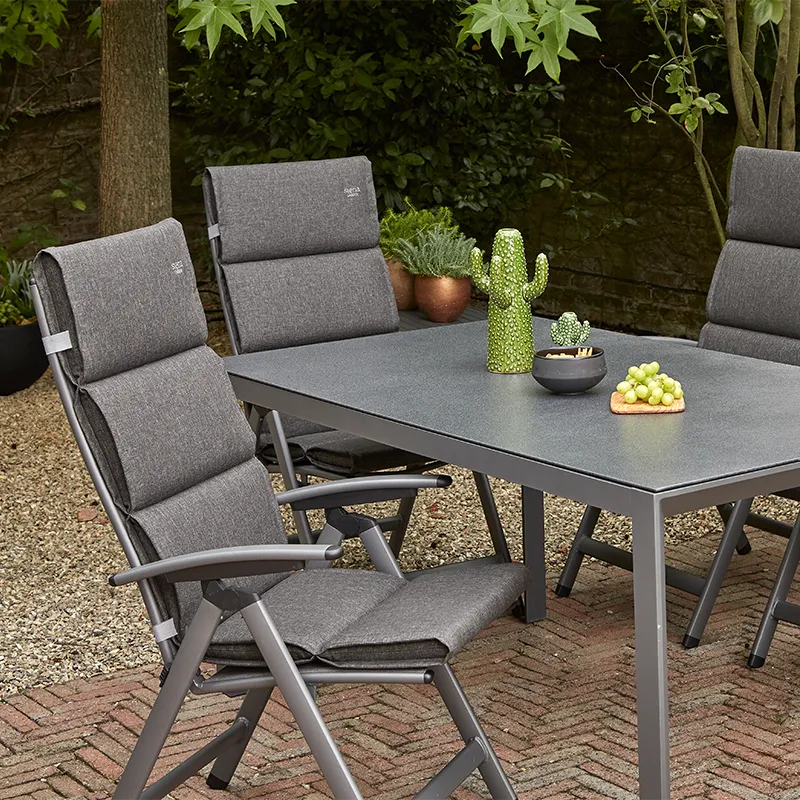 Drei Gartensessel in anthrazit mit dunkelgrauen Sitzauflagen mit horizontalen Steppnähten um einen grauen Tisch auf Kiesfläche im schattigen Garten.
