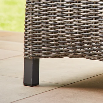 Detailaufnahme eines grauen Geflecht Stuhlbeins auf einer hellen Terrassenplatte.