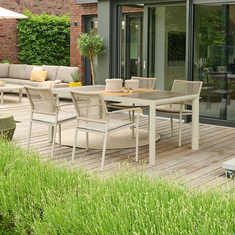 Moderne Outdoor Essgruppe mit hellen Geflechtstühlen und rechteckigem Tisch auf einer Holzterrasse vor einem Haus mit Lounge Sofa und Pflanzen.