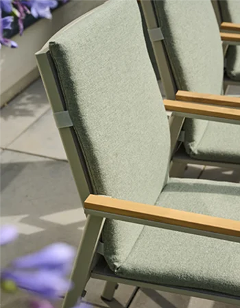 Hellgrüne gepolsterte Stuhlauflage mit strukturierter Oberfläche auf einem Stuhl mit Holzarmlehnen im Außenbereich.