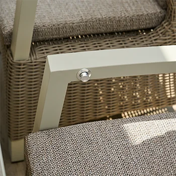 Detailaufnahme eines Gartenstuhls aus beigem Geflecht mit gepolstertem Sitzkissen und hellem Metallrahmen.k