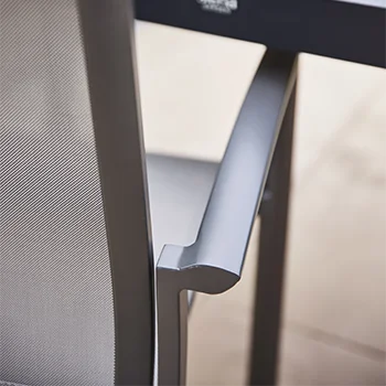 Nahaufnahme der Armlehne eines Gartenstuhls aus dunkelgrauem Metall mit feinmaschiger Rückenbespannung, neben einer Tischkante.