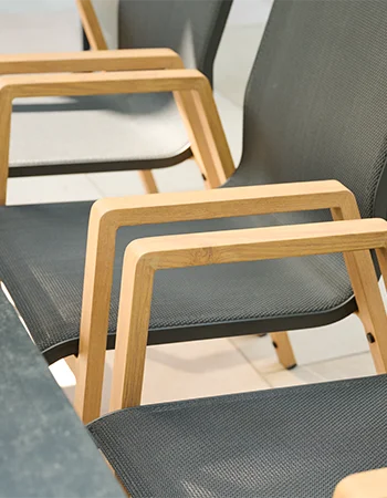 Detailansicht moderner Gartenstühle mit Armlehnen in Holzoptik und dunkelgrauem Textilgewebe neben einem Outdoor Tisch.