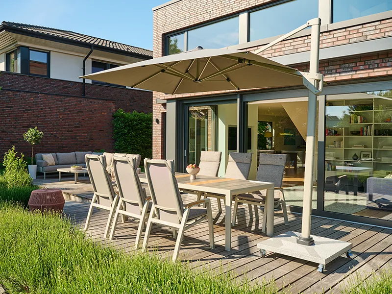 Garten-Sitzgruppe unter Ampelschirm, dahinter Gartenlounge auf Holzterrasse. Von grünen Rasen umgeben.