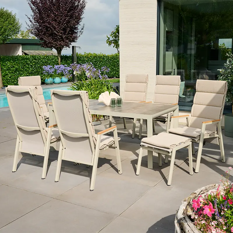 Outdoor Essgruppe mit hellen Hochlehnern und grauem Esstisch auf einer Terrasse neben Pool und blühenden Pflanzen.